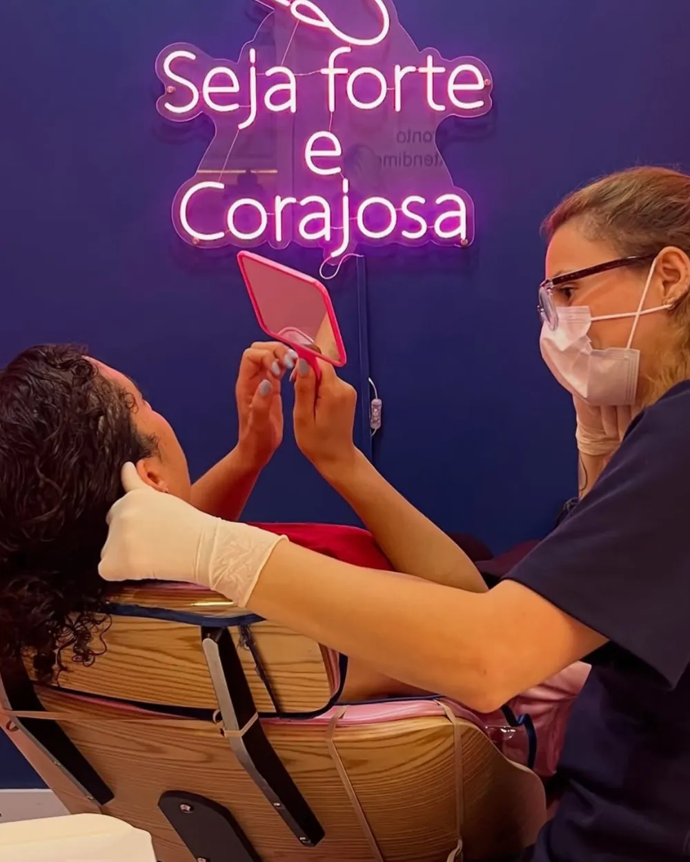 Perfuradora da Dra. Piercing a mostrar o resultado à cliente, sob o néon «Seja forte e corajosa»